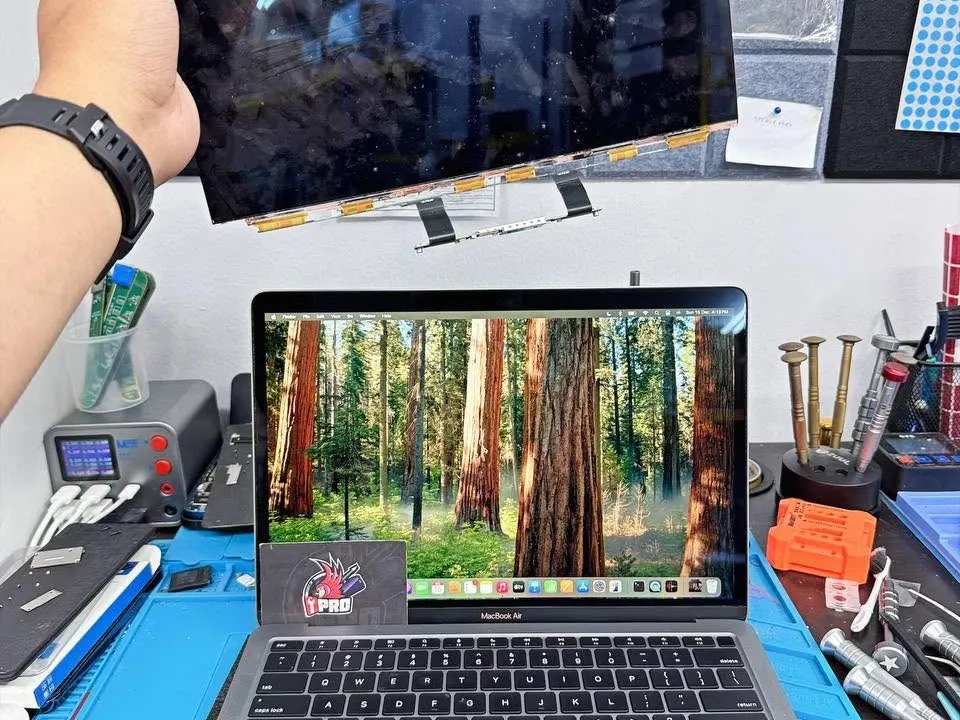 Technician holding a replacement MacBook display panel above the Mac on the counter